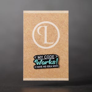 May include: A rectangular brown card with a white circular design and the letter "T". A black and teal pin with the text "MY CODE Works! (I HAVE NO IDEA WHY)" is attached to the card.
