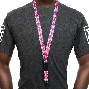 Könnte beinhalten: Ein Schlüsselband mit Union Jack-Flaggenmuster in Rot, Weiß und Blau. Das Schlüsselband wird um den Hals getragen. Die Person trägt ein dunkelgraues T-Shirt mit weißem Text auf den Ärmeln.