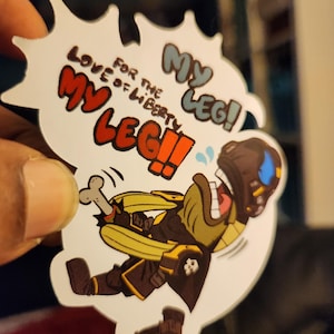 May include: A white sticker with a cartoon character holding a bone and running. The character is wearing a black and yellow outfit and a helmet. The sticker has the text "FOR THE LOVE OF LIBERTY MY LEG!" in a speech bubble.