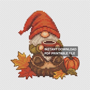 Puede incluir: Un patrón de punto de cruz que muestra un gnomo con un gran sombrero naranja, sosteniendo una taza oscura y sentado junto a una calabaza y hojas de arce. El texto INSTANT DOWNLOAD PDF PRINTABLE FILE está superpuesto en la imagen.