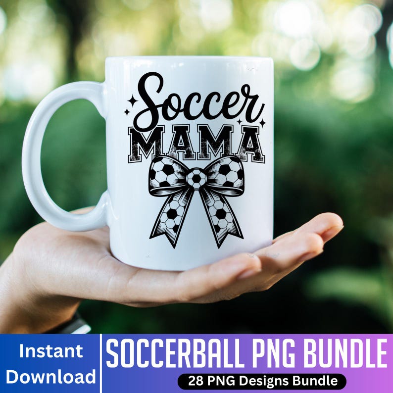 May include: White ceramic mug with the words "Soccer MAMA" in black script and block letters, with a soccer ball bow design. The mug is held in a hand against a blurred green background.