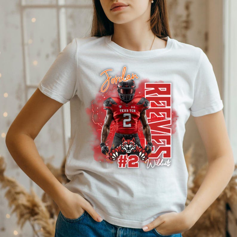 K&ouml;nnte beinhalten: Wei&szlig;es T-Shirt mit einem Footballspieler in roter und schwarzer Uniform. Das Shirt zeigt den Namen "Jordan" in Schreibschrift, die Nummer "2" und das Wort "Reeves". Unten befindet sich ein rotes und schwarzes Wildcat-Logo.