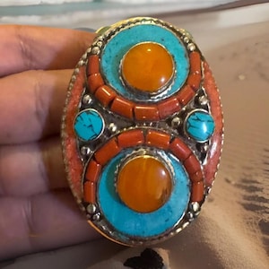May include: A silver ring with turquoise and coral stones. The ring has a circular design with two amber stones in the center.