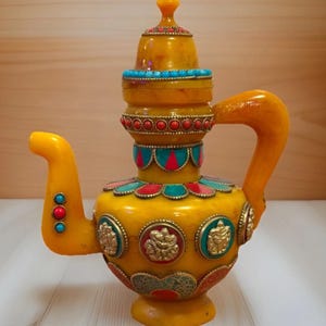 May include: Ornate yellow teapot with decorative turquoise and red accents. The teapot features a detailed design with gold-colored embellishments and a matching lid. A unique piece for home decor.