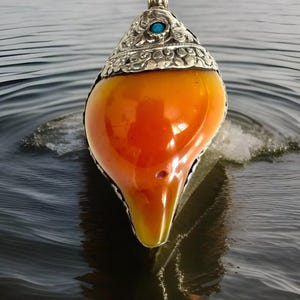 巻き貝とマンゴーの形をしたチベットの縁起の良い花のシンボルが手彫りされたゴージャスでユニークな琥珀色のペンダント。高さ4インチ、重さ75グラム。