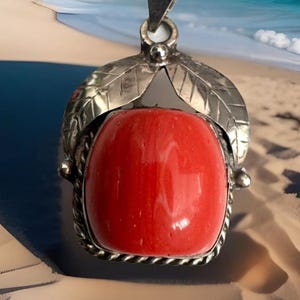 May include: A silver pendant with a red coral stone set in a silver bezel. The pendant features two silver leaves on either side of the stone.