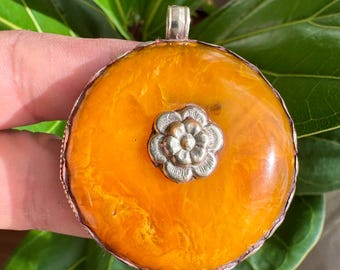 Pingente deslumbrante, tradicional tibetano, em prata e resina de âmbar copal, com entalhes florais auspiciosos feitos à mão por toda a sua extensão. Mede 5,8 cm de altura e pesa 38 gramas.