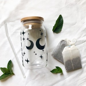 May include: A glass bottle with a bamboo lid and a black and white design of moons and stars. The bottle is accompanied by two tea bags and a glass straw.