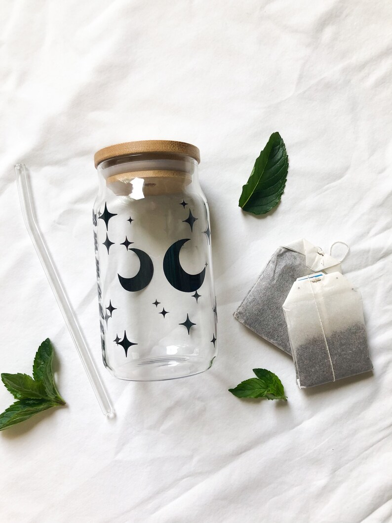 May include: A glass bottle with a bamboo lid and a black and white design of moons and stars. The bottle is accompanied by two tea bags and a glass straw.