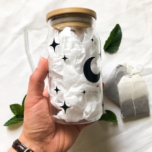 May include: A clear glass bottle with a wooden lid and a moon and stars design. The bottle is filled with white tissue paper.