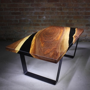 May include: A wooden coffee table with a black epoxy resin inlay. The table has a natural wood finish and black metal legs.