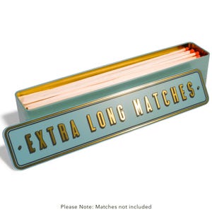 May include: A teal metal matchbox with a gold interior and a lid displaying "EXTRA LONG MATCHES" in gold. The box is open, showing long, white matches with red tips. The box is rectangular.