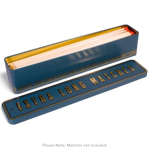 May include: A navy blue metal matchbox with a gold interior and lid. The lid is inscribed with "EXTRA LONG MATCHES" in gold lettering. The box contains extra-long matches with red tips. The text "Please Note: Matches not included" is at the bottom.