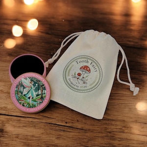 May include: A pink metal Tooth Fairy keepsake box with a fairy illustration, open next to a drawstring bag with a mushroom design and the text "Tooth Fairy". The items are on a wooden surface.