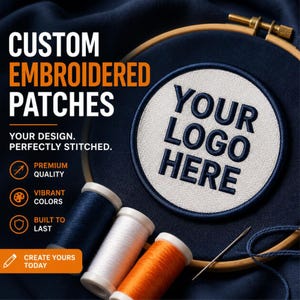 Puede incluir: Un bastidor de bordado circular de madera sostiene una tela azul oscuro con un parche circular blanco que presenta el texto YOUR LOGO HERE bordado en azul oscuro. Tres carretes de hilo azul, blanco y naranja están cerca con una aguja.