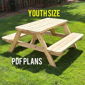 May include: A light-colored wooden picnic table with attached benches, designed for youth size. The image features the text YOUTH SIZE at the top and PDF PLANS at the bottom. The table has a slatted top and angled legs for stability.