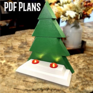 May include: A wooden Christmas tree with a white base and two red tea lights. The tree is made of four green triangular pieces stacked on top of each other. The base has a tiered design.  PDF Plans.