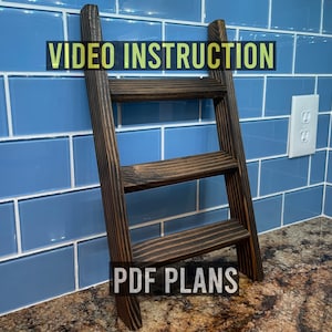 May include: A dark brown wooden ladder shelf with three shelves. The shelf is leaning against a blue tiled wall. The text "VIDEO INSTRUCTION" and "PDF PLANS" is printed on the image.