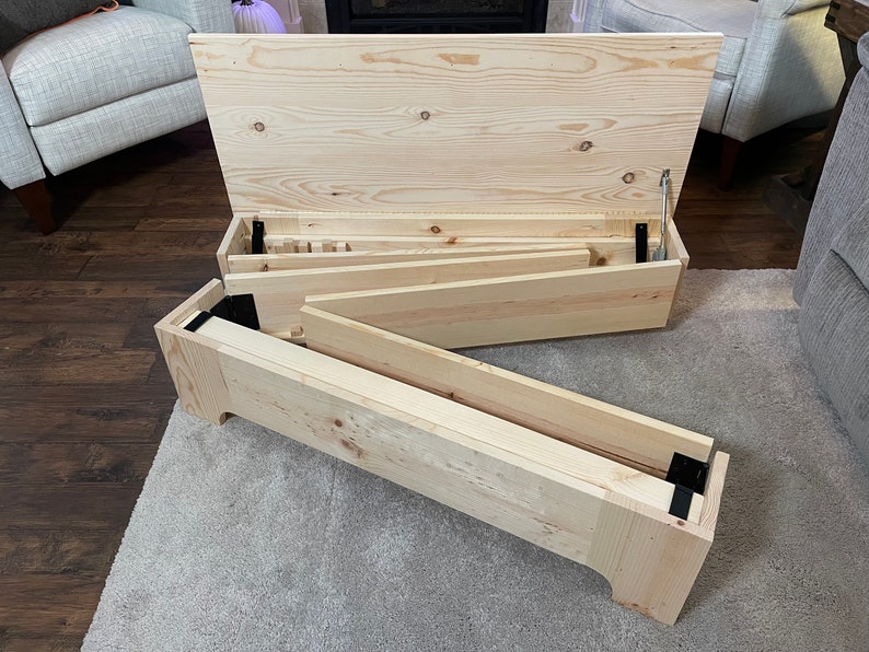 K&ouml;nnte beinhalten: Eine Holzkiste mit einem Scharnierdeckel, ge&ouml;ffnet, um eine Reihe von Holzregalen im Inneren zu zeigen. Die Kiste ist aus unbehandeltem Kiefernholz gefertigt und hat schwarze Metallscharniere.