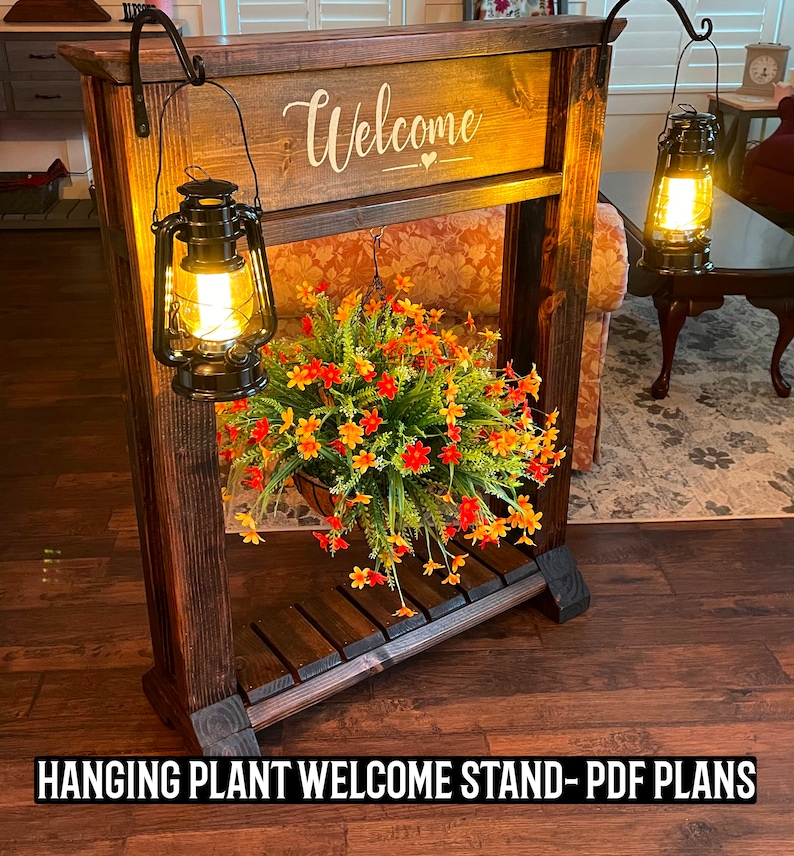 May include: A wooden hanging plant stand with a welcome sign and two black lanterns. The stand has a shelf and is decorated with a hanging plant with orange and yellow flowers.