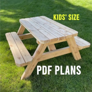 May include: A wooden picnic table designed for kids, with a natural wood finish. The table is shown on a grassy lawn. The text "KIDS' SIZE" and "PDF PLANS" is visible in the image.