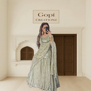 Puede incluir: Un atuendo formal verde claro con adornos de lentejuelas plateadas. El atuendo incluye una falda larga, una blusa y un chal drapeado. La imagen también muestra el texto "Gopi Creationz".