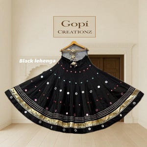 May include: Black lehenga skirt with gold and silver trim, adorned with colorful circular embellishments. The skirt has a wide, flowing design and is displayed on a hanger. The brand name "Gopi Creationz" is visible.