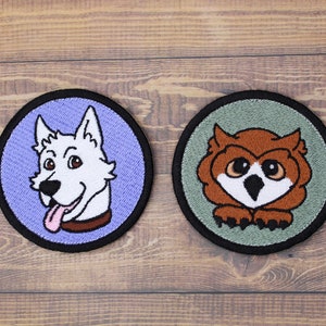 May include: Two embroidered patches, one with a white dog with a pink tongue and a brown collar on a purple background, and the other with a brown owl with yellow eyes on a green background.