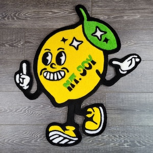May include: A yellow lemon-shaped rug with a green leaf and a smiling face. The rug has the text "MT. JOY" written on it.