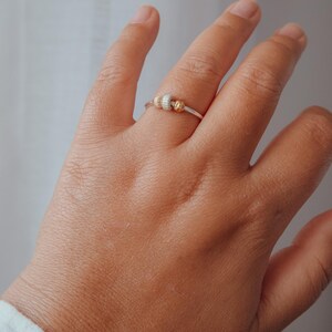 May include: A silver ring with three decorative beads. The beads are gold and silver in color. The ring is on a person's hand.