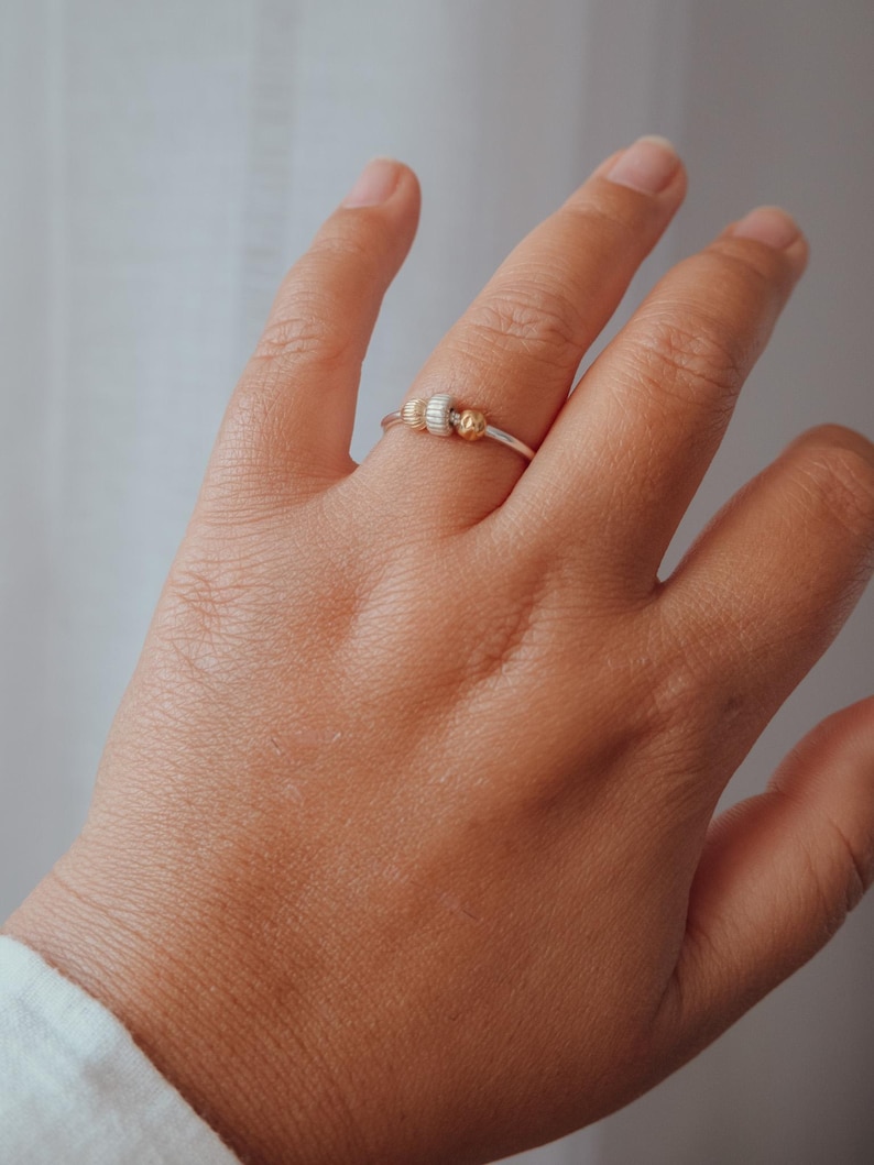 May include: A silver ring with three decorative beads. The beads are gold and silver in color. The ring is on a person's hand.