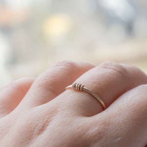 May include: A simple gold ring with a twisted band design. The ring is worn on a person's finger.