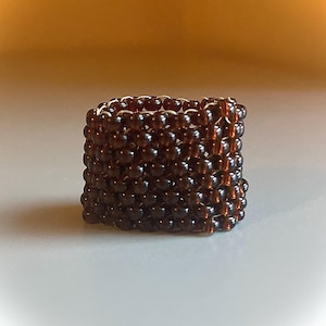 May include: A brown beaded ring made of small, round beads woven together in a square pattern.