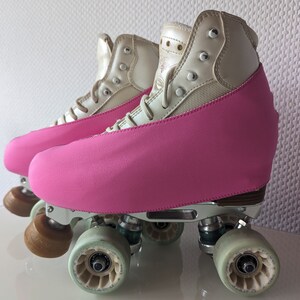 Op de afbeelding: Een paar witte rol schaatsen met roze laarzenhoezen. De schaatsen hebben zilveren frames en wielen.