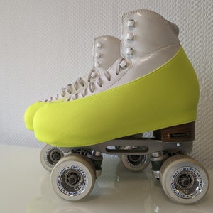 Op de afbeelding: Een paar witte rol schaatsen met neon gele laarzenovertrekken. De schaatsen hebben zilveren frames en zwarte wielen met blauwe en witte letters die "Roll-Line Giotto 500" lezen.
