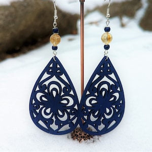 May include: A pair of navy blue wooden earrings with a delicate floral cutout design. Each earring features a round, light brown bead.