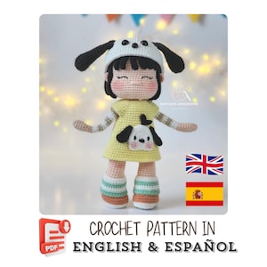 May include: A handmade crochet doll wearing a yellow dress with a dog face applique, a white hat with black ears, and striped socks. The doll has black hair and is holding its arms out. The image includes the text "CROCHET PATTERN IN ENGLISH & ESPAÑOL".