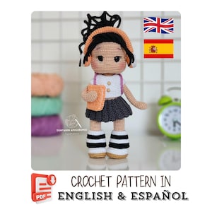 May include: A handmade crochet doll, dressed in a white shirt, gray skirt, and black and white striped boots, holding an orange book. The doll has black hair with an orange headband. The image includes text that says "CROCHET PATTERN IN ENGLISH & ESPAÑOL."