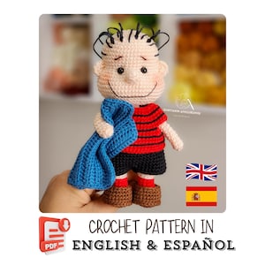 May include: A handmade crochet doll of a cartoon character, dressed in a red and black striped top, black shorts, and brown shoes, holding a blue blanket. The text "CROCHET PATTERN IN ENGLISH & ESPAÑOL" is displayed.