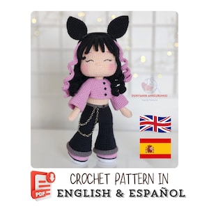 May include: A handmade crochet doll with black hair, wearing a pink crop top, black pants, and a black headband with bunny ears. The doll has a chain belt and is wearing black shoes. The text "CROCHET PATTERN IN ENGLISH & ESPAÑOL" is at the bottom.