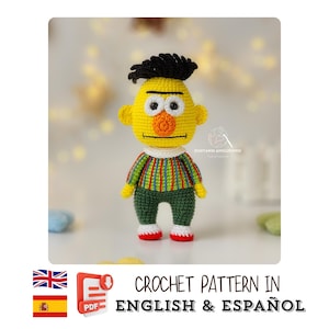 May include: A crocheted doll resembling a cartoon character. The doll features a yellow head, black hair, and is dressed in a striped top, green trousers, and red-trimmed shoes. The image includes text that reads "CROCHET PATTERN IN ENGLISH & ESPAÑOL".