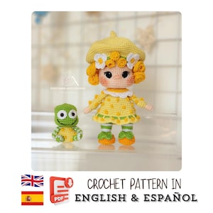 May include: A crochet doll wearing a yellow beret with white flowers and a yellow dress with small yellow dots, paired with green and white striped socks and orange shoes. Beside the doll is a small green and yellow crochet frog figure.