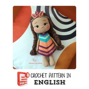 Può includere: Schema all'uncinetto in inglese per una bambola con capelli castani, un vestito colorato e una fascia con foglie. La bambola è seduta su un cuscino a strisce bianche e nere. Il testo "CROCHET PATTERN IN ENGLISH" è sotto l'immagine.