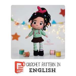 May include: Crochet pattern for a green and black amigurumi doll with a pink bow and colorful beads in her hair. The pattern is available in PDF format and is written in English.  "CROCHET PATTERN IN ENGLISH" and "PDF" are written on the image.