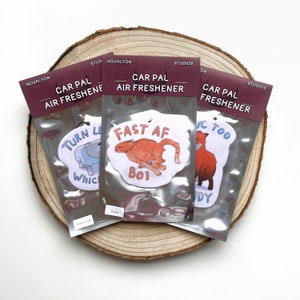 May include: Three car air fresheners with humorous animal illustrations and text. The first air freshener features a blue dog with the text "Turn Least AF". The second air freshener features an orange cat with the text "Fast AF Boi". The third air freshener features a red fox with the text "IC Too DY".