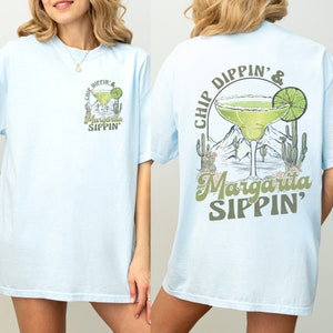 May include: Light blue t-shirt with a graphic of a margarita glass with a lime wedge and the text "Chip Dippin' & Margarita Sippin'" on the front and back.
