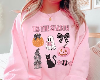 May include: Pink sweatshirt with the text "TIS THE SEASON" and Halloween-themed graphics. The graphics include a pumpkin, ghost, bow, pink pumpkin, haunted house, black cat, and candy.