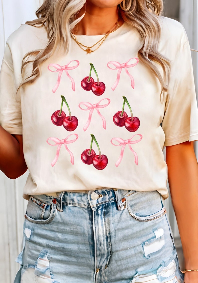 May include: A cream-colored t-shirt with a graphic of pink bows and red cherries.