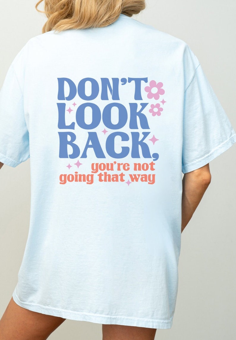 May include: Light blue t-shirt with the text "Don't look back, you're not going that way" in blue and pink lettering with flowers and stars.