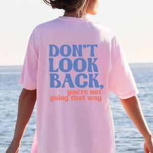 May include: Pink oversized t-shirt with the text "DON'T LOOK BACK. you're not going that way" in blue and orange lettering.